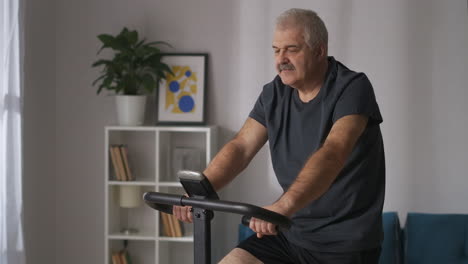 Un-Hombre-De-Mediana-Edad-Está-Entrenando-Con-Una-Bicicleta-Estática-En-Un-Entrenamiento-Cardiovascular-En-Casa-Manteniendo-La-Actividad-Física-En-Autoaislamiento